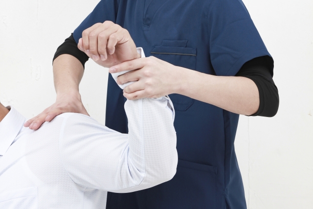 整体施術者が患者の腕を他動的に上げ、可動域を広げるための施術を行っている写真。
