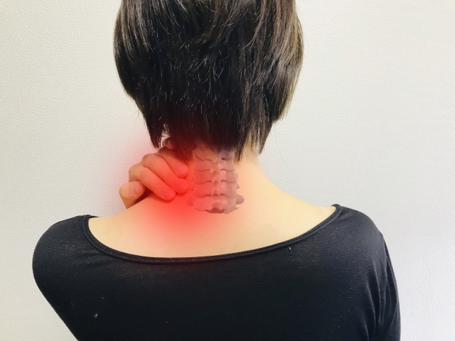 首の後ろを押さえ、こりや痛みを訴える女性の写真。頸椎部分に赤みの表現あり