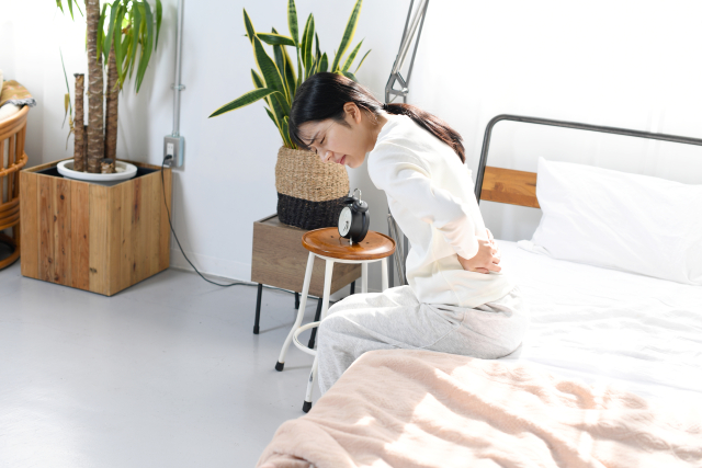 慢性的な腰痛に悩み、ベッドの上で腰を押さえる女性