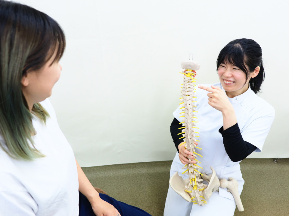 施術スタッフが背骨の模型を使って女性に説明をしている写真